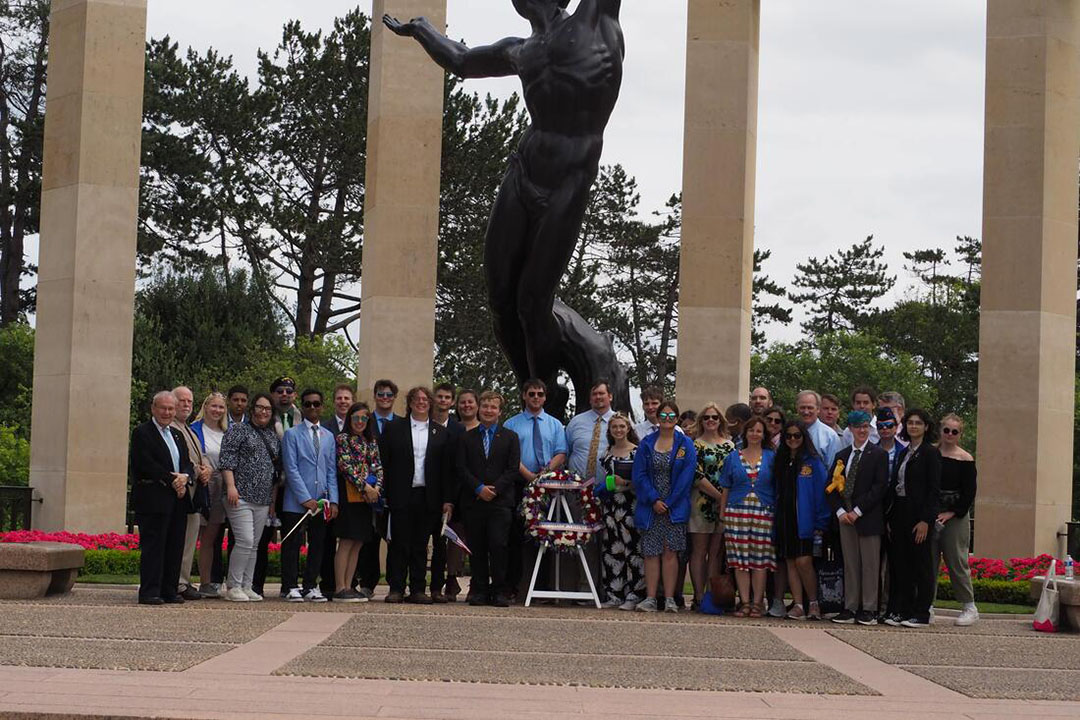 A group of students standing outside at a stone monument with columns and a statue