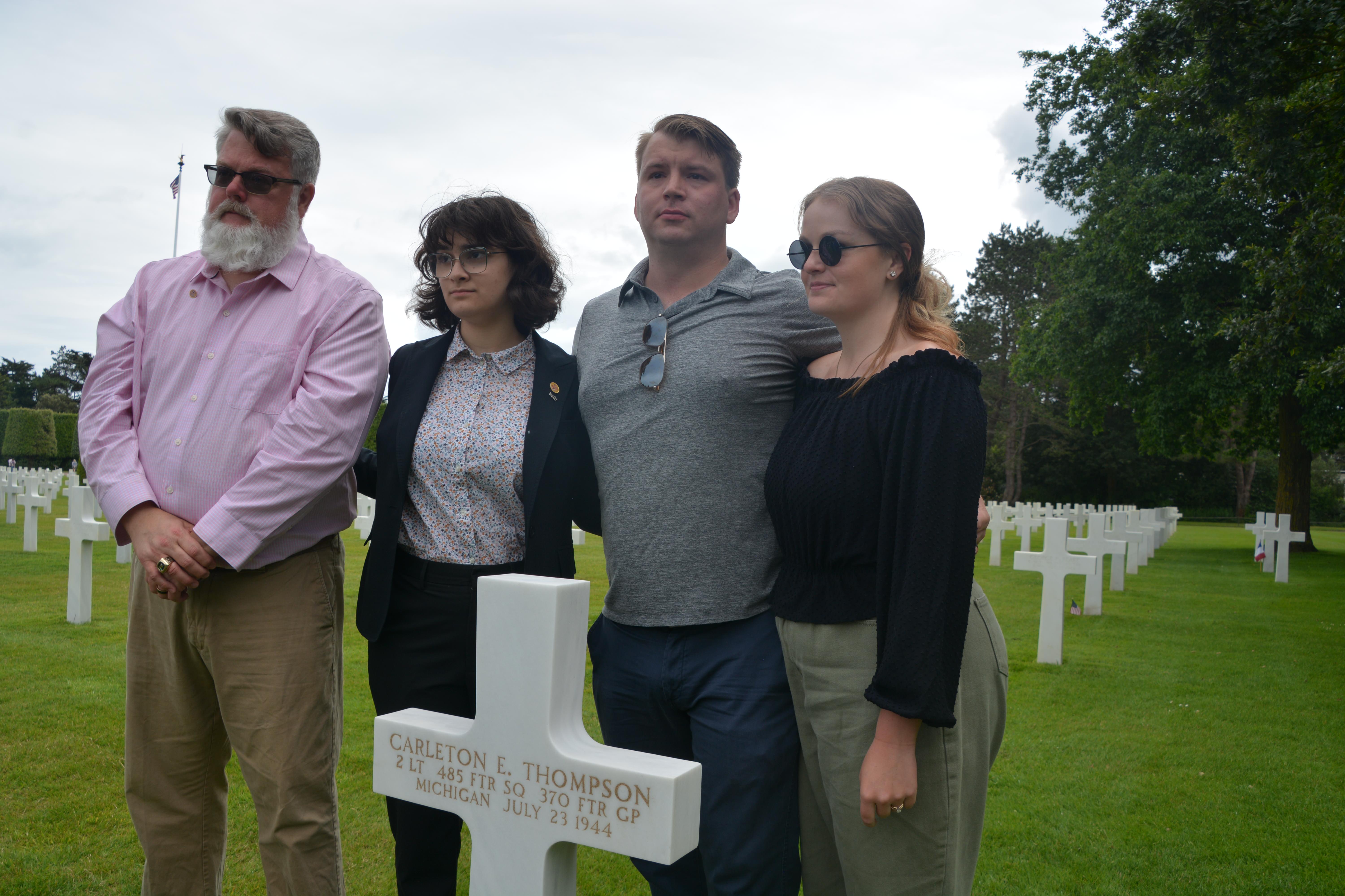 People standing with cross headstone in Normandy American Cemetery