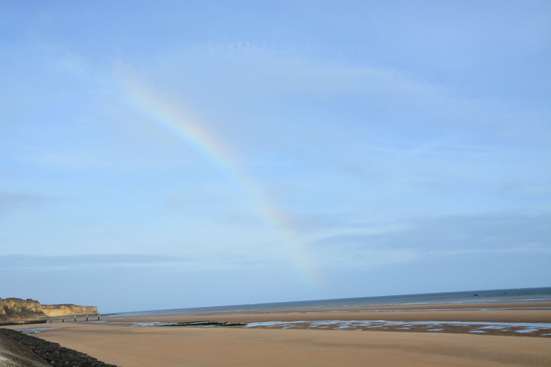 A rainbow in a blue sky over a sandy beach