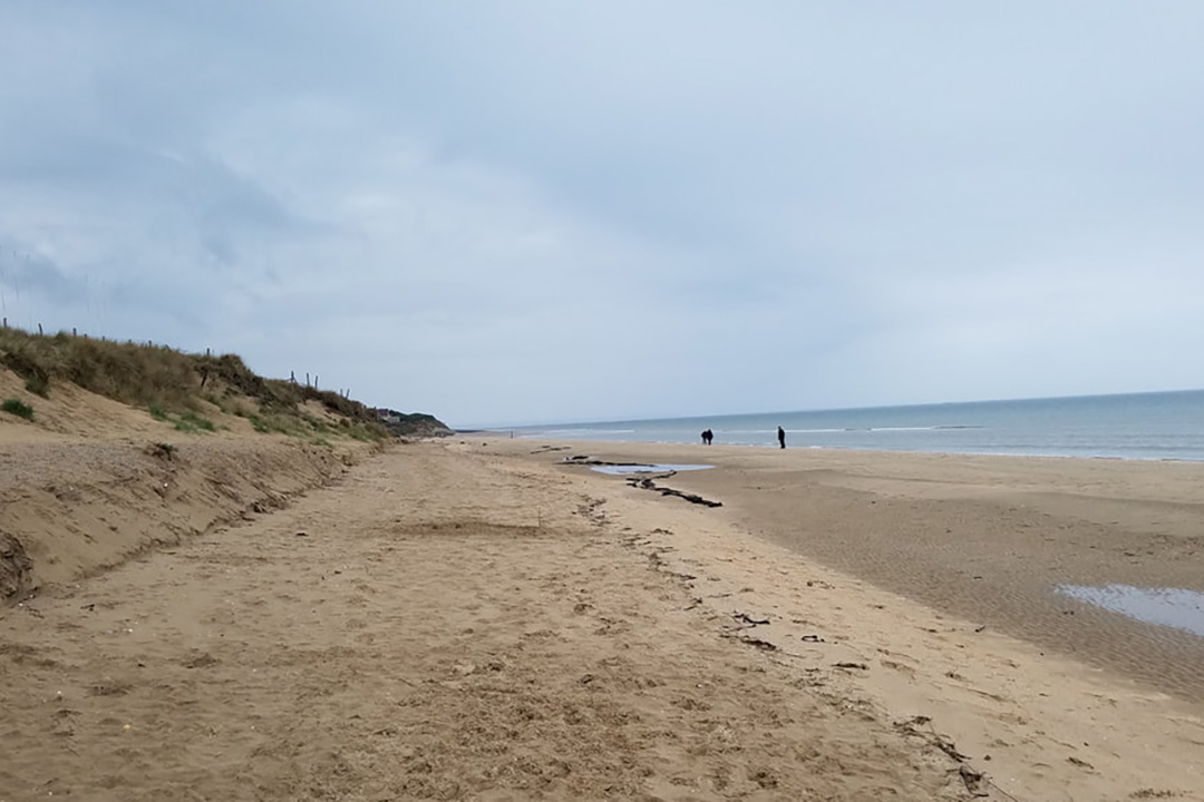 A view of a beach under a cloudy sky, with two distant figures walking on the sand