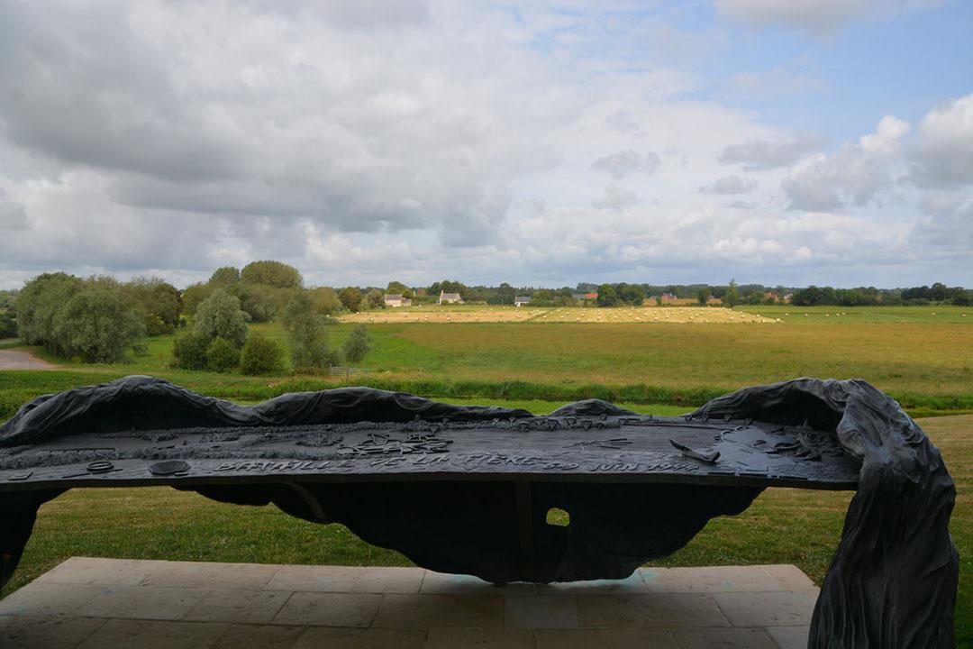 A black stone relief carving with words and scenes from a battle, in a country field