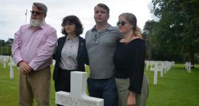 People standing with cross headstone in Normandy American Cemetery